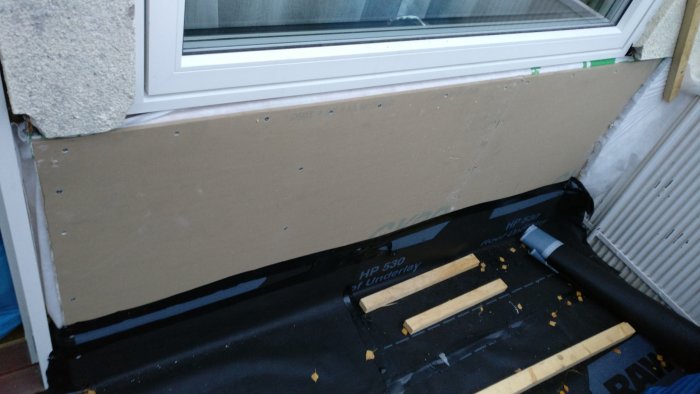Oskyddad fasad med synlig vattentätning och byggmaterial på balkong i väntan på puts.
