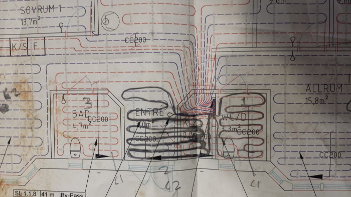 Sliten ritning av en värmesysteminstallation med markerade rördragningar i olika färger och handskrivna noteringar.