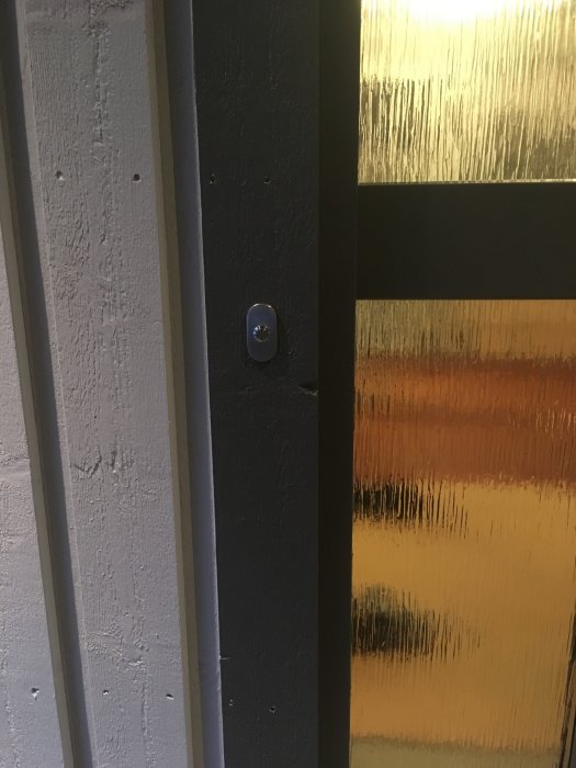 Nyinstallerad ringklockeknapp på en grå vägg vid sidan av en dörr med gulfärgat glas.