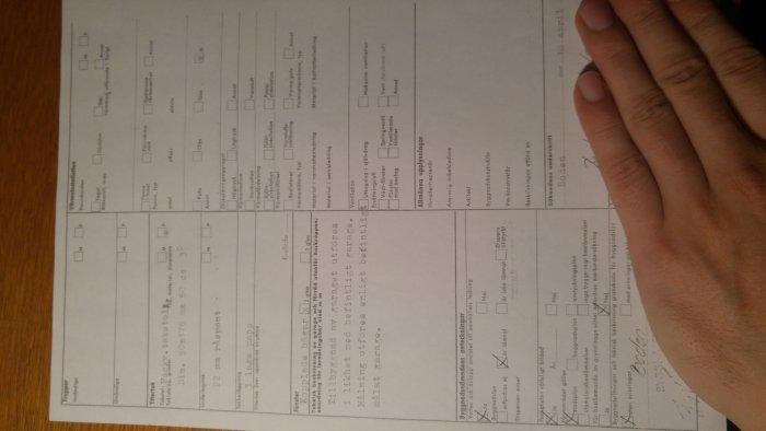 Hand håller ett papper med arkitektoniska planritningar och anteckningar i oskarp fokus.