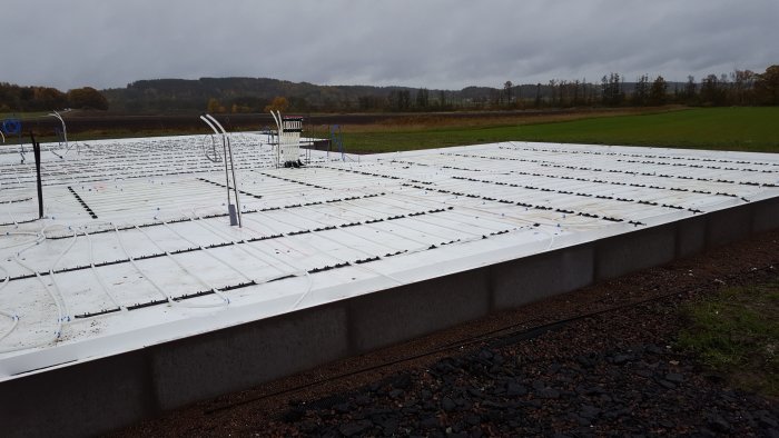 Grundarbete för byggprojekt med installation av värmeslingor på isoleringsplattor under gråmulen himmel.