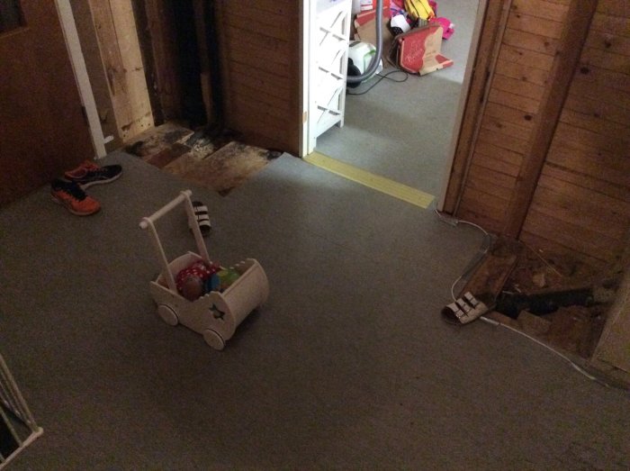 Interiör av en hall med ett barnvagnsleksak, skor och en synlig del av ett bjälklag.