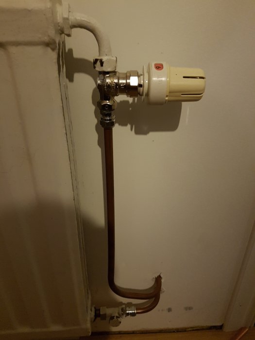 Nyinstallerad radiator med termostat och kopparledningar mot vit vägg.