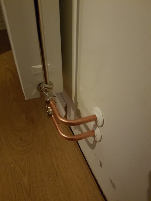 Nyinstallerade kopparrör kopplade till en vit väggradiator i ett hörn.