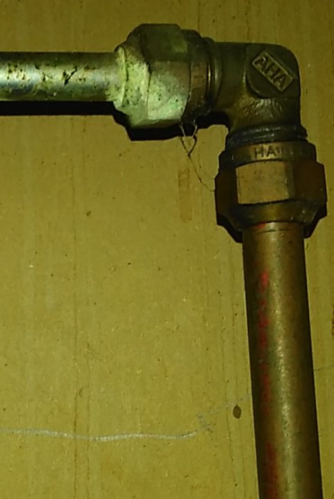 Metallrör med kopplingsbeslag mot en brun bakgrund, möjligen en del av VVS-installation.