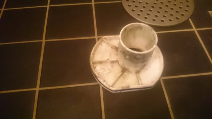 Lös del av en golvbrunn på kaklat golv bredvid en hel brunn med förvirring angående installation.