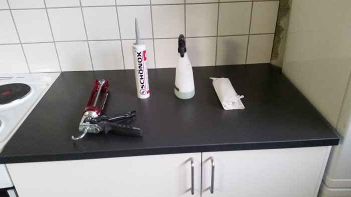 Köksbänk med fogmassa, fogpistol, sprayflaska och papper förberedda för silikonfogning.