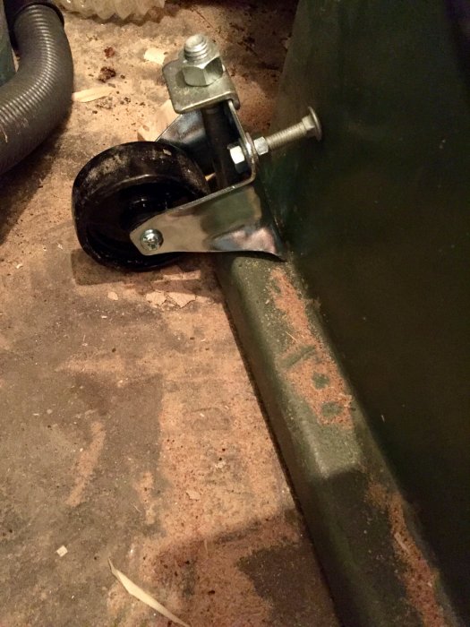 Hjul och fäste monterat på grön stålstruktur med en synlig bult som distans.