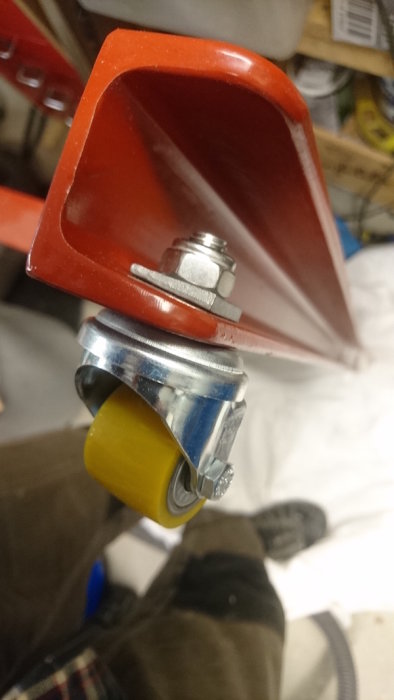 Närbild på ett litet gult hjul monterat på en röd rams struktur, avsett för en såg, i en verkstadsmiljö.