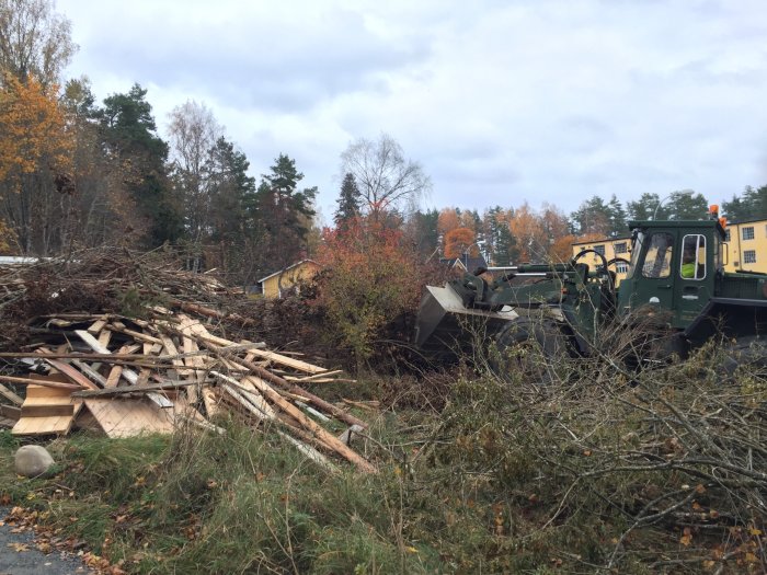 Hög med kvistar och byggavfall bredvid grön militärliknande lastbil under hösten.