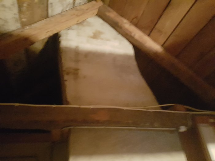 Takstol som ligger an mot en murstock i ett mörkt vindutrymme, belyser ett byggfel.