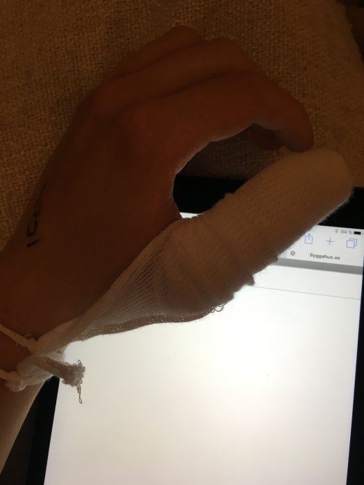 Hand med bandage vid surfplatta som visar en webbsida med bygghusrelaterat innehåll.