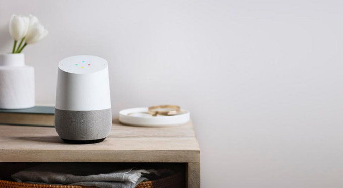 Google Home smart högtalare på en trähylla bredvid en vit vas med tulpan och en vit tallrik.