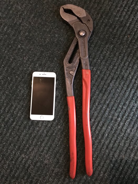 Knipex tång bredvid en iPhone på en mörk textilmatta.