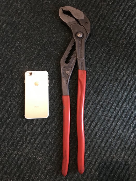 Knipex tång med röda handtag bredvid en iPhone på en mörk textilmatta.