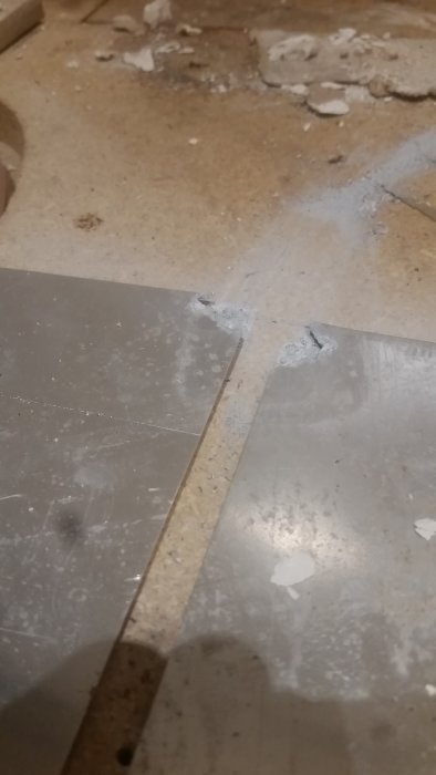 Golv under renovering med synlig skada och korrosion på golvvärmeplåtar.