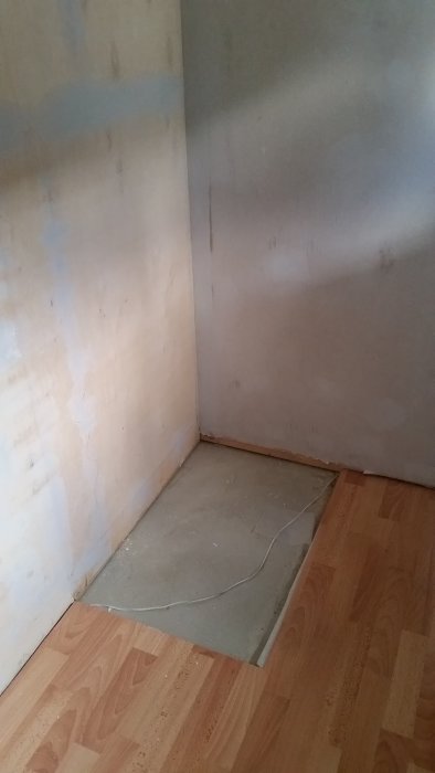 Hörn av ett rum med exponerad betongplatta och intilliggande laminatgolv.