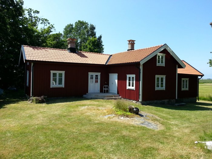 Rött svenskt hus med vita PVC-fönster och tegeltak mot en lantlig sommarbakgrund.