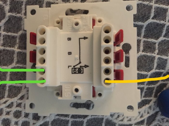 Transistordimmer med trådar markerade i grönt och gult enligt beskrivningen, ligger på ett mönstrat tyg.