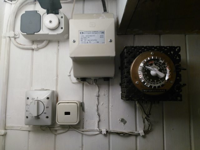 Gamla elektriska installationer på en vägg, inklusive termostat, transformator, uttag och motorvärmartimer.