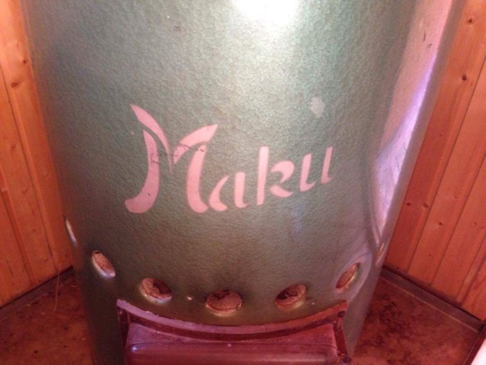 Närbild av ett bastuaggregat med märkesnamnet "Maku" på framsidan, placerat i en träbeklädd bastu.