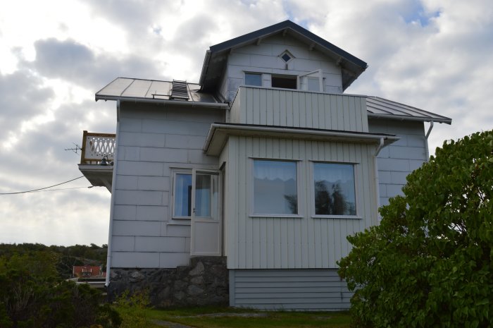 Ett tvåvåningshus med lutande tak och luftledning framför en himmel med moln.