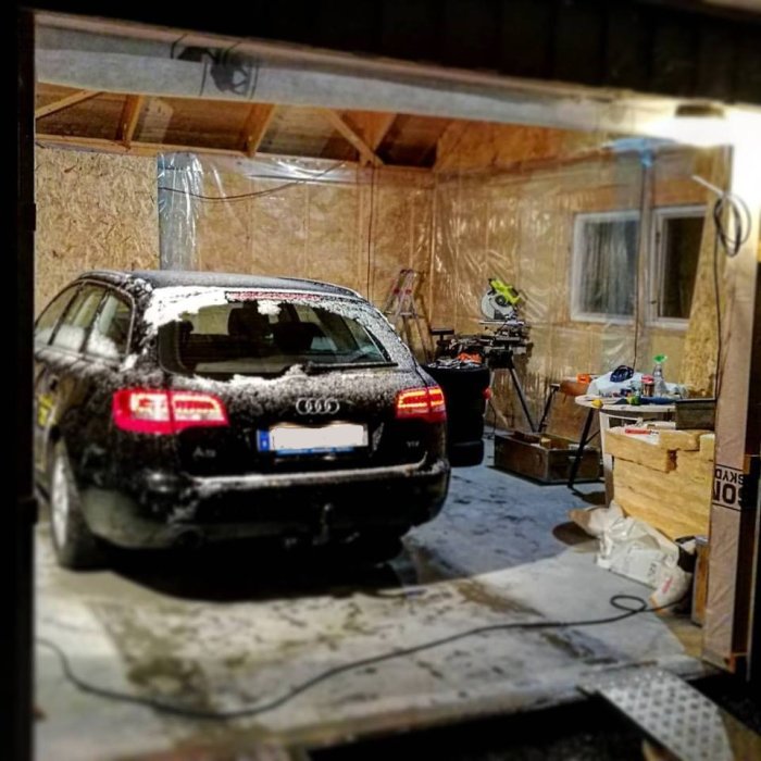 Snedbild av en Audi parkerad i ett garage med byggarbetsmaterial och snö på bilen.