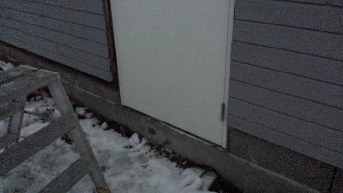 Vit garagedörr i glugg med leca vid basen och träpanel ovanför, skillnad i djup synlig.