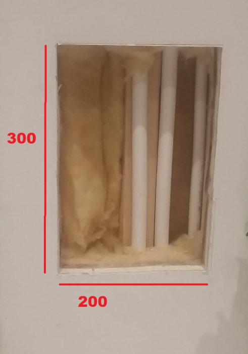 Öppning i vägg med synliga vattenrör och isolering, märkt för en framtida inspektionslucka på 200x300 mm.