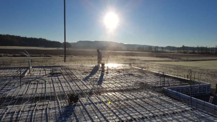 Solnedgång över en nygjuten betongplatta med armeringsjärn och byggarbetsmaterial.