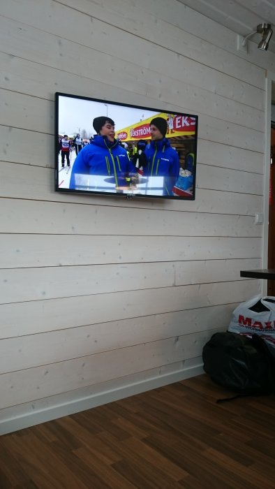 Två personer i sportkläder syns på en TV som är monterad på en trävägg i ett rum.