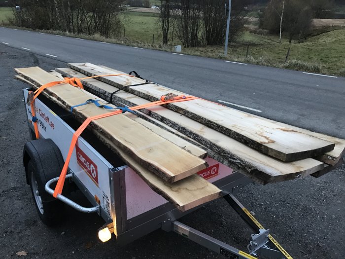 Ek- och askplank fastspända på en släpvagn vid vägkanten.