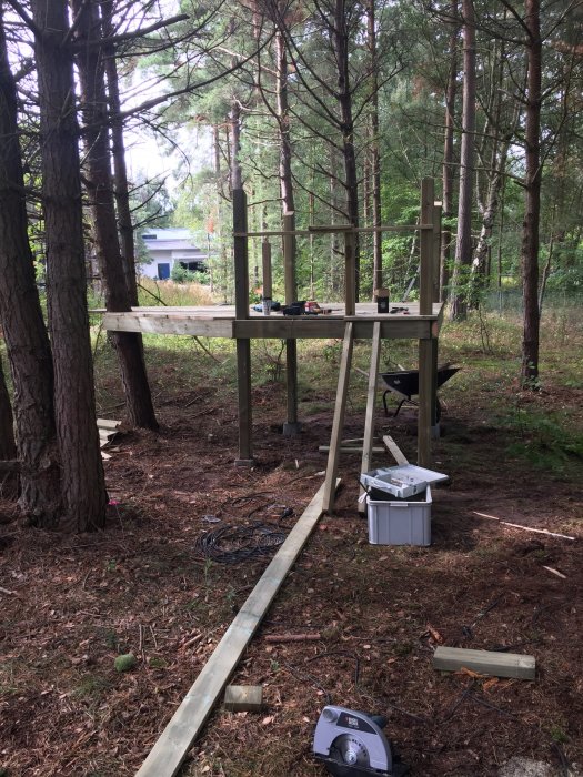 Konstruktion av piratskeppsinspirerad lekstuga på pålar i skogsmiljö med verktyg och byggmaterial på marken.