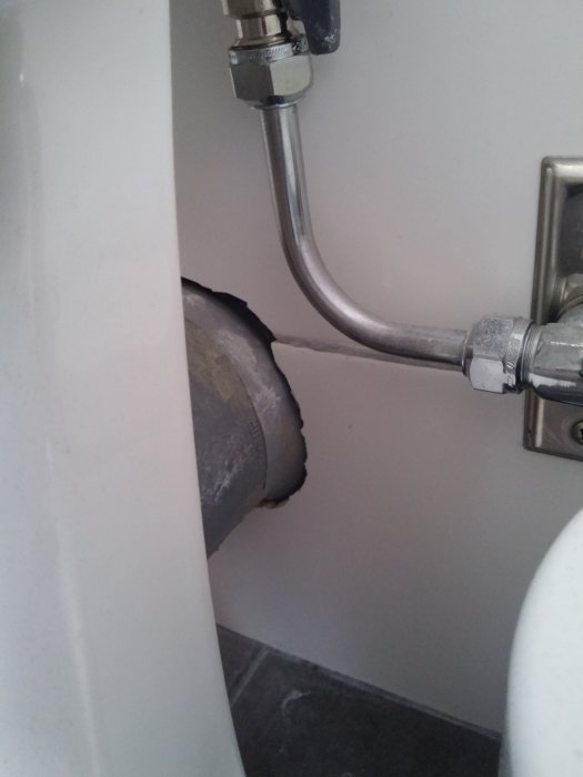 Toalettrör anslutet till väggen utan synlig muff, omgivet av kantigt kakel och en toalettstol.