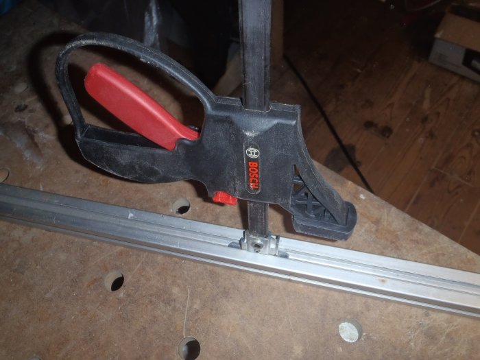 T-track med en fastspänd tving från Bosch i en arbetsmiljö.