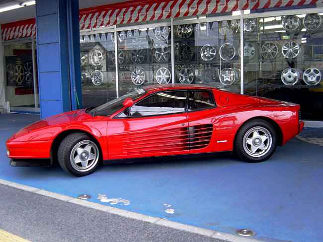 Röd Ferrari Testarossa parkerad framför en butik med fälgar.