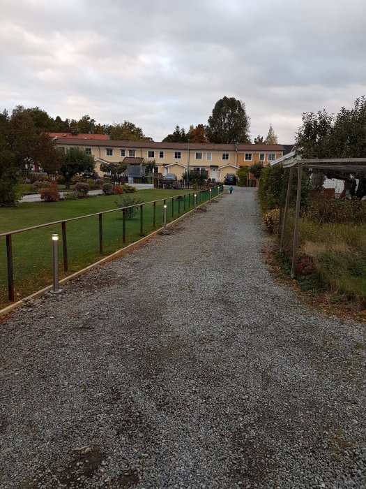 Grusväg som leder till gula radhus med nyinstallerade stolplyktor som lyser längs sidan.