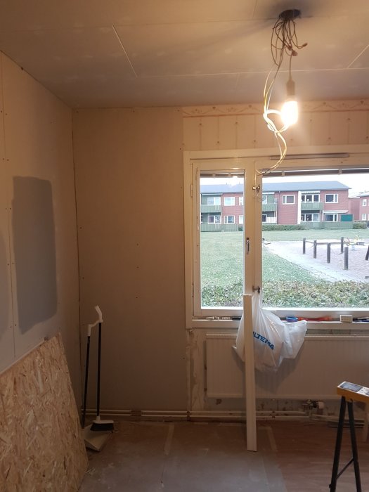 Ett rum under renovering med nya renoveringsgipsplattor installerade runt ett fönster.