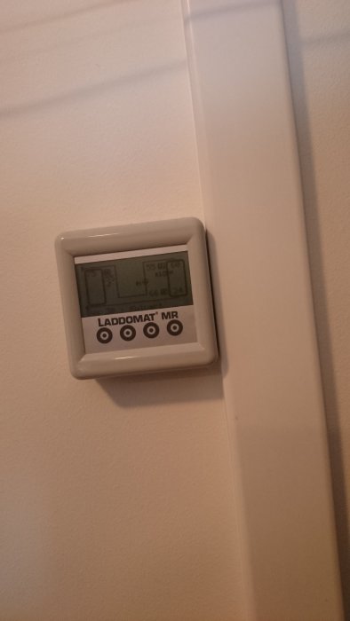 Värmeregulatorns display visar temperaturer, monterad på en vägg intill en vit dörrkarm.