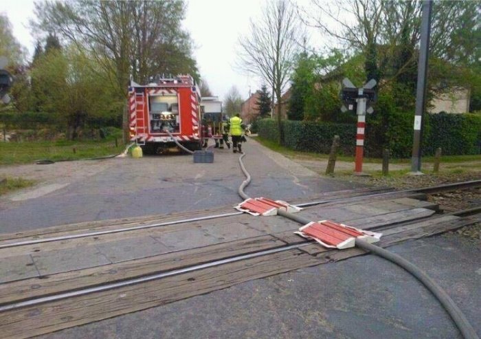 Brandbil vid järnvägsövergång med slangar över spåren och brandmän i bakgrunden.