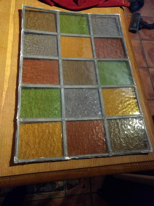 Blyinfattad mosaikrutor i olika färger som visar tecken på bågformning, placerade på ett bord.