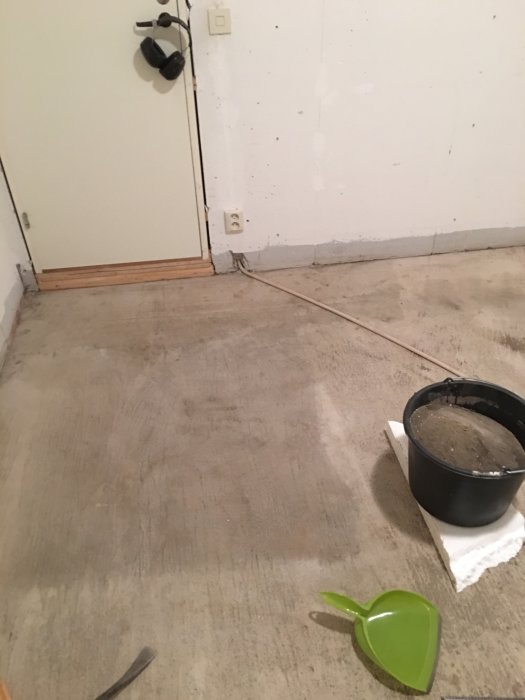Bild på avlägsnat golv i ett förråd med fuktiga sandfläckar synliga och renoveringsmaterial.