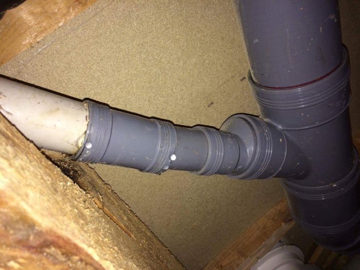 Läckande grått och vitt avloppsrör i tak, synlig skarv där det vita möter det gråa röret.