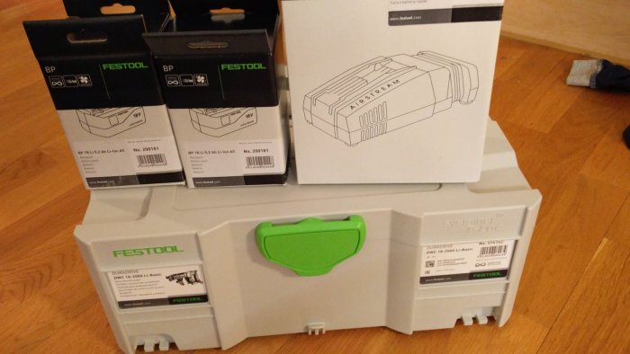 Nya Festool verktyg och batteripaket i originalförpackning på trägolv.