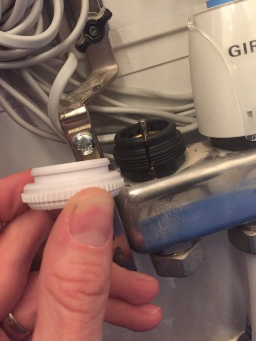 Hand håller en grå gängad ring framför en svart ring installerad på en ventil med ställdon i bakgrunden.