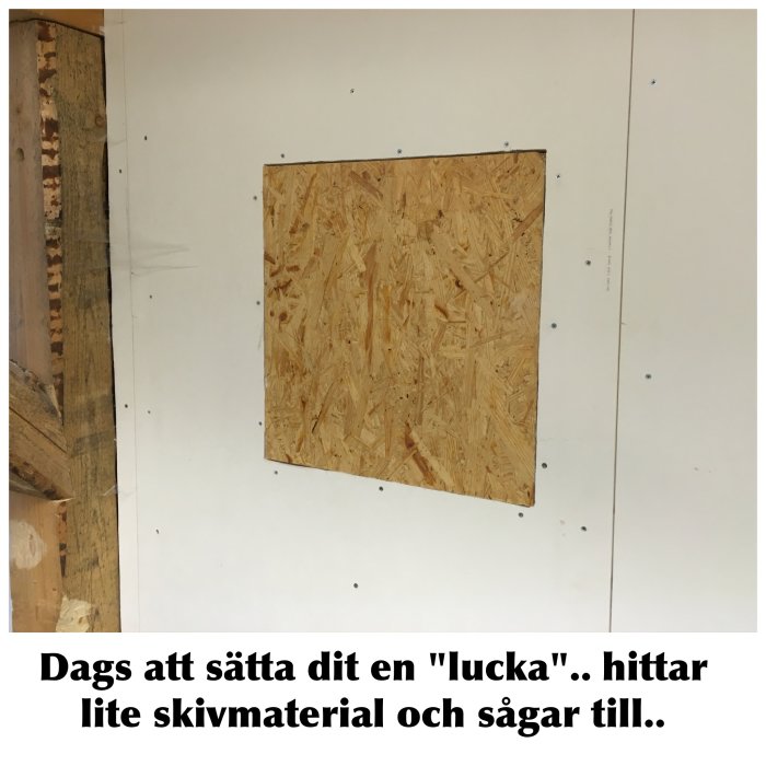 OSB-skiva monterad i kvadratisk öppning i en vit garagevägg, förberedelse för "tavla".