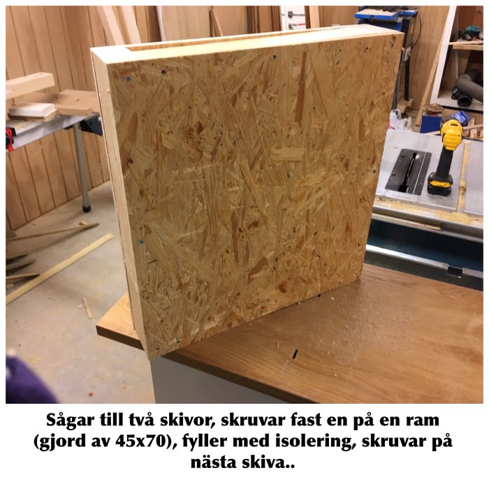OSB-skiva fastskruvad på träram syns i en verkstad, verktyg och timmer i bakgrunden.