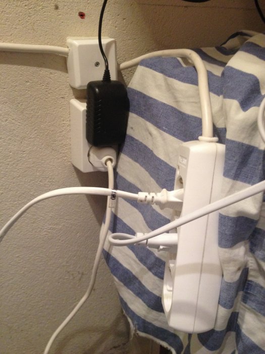 Oorganiserad elinstallation med överbelamrat vägguttag och synliga sladdar över en handduk.