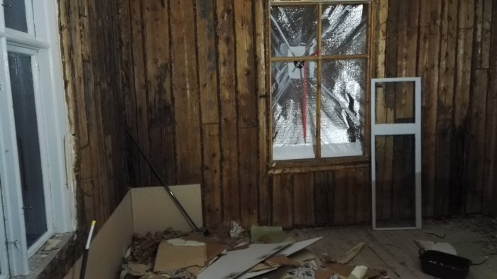 Renoveringsarbete med synlig timmerstomme, rivet ytskikt och fönster på golv i ett gammalt hus.
