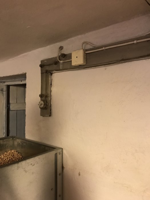 Svart elledning kopplad till en lampa längs en vit vägg över ett metallskåp.